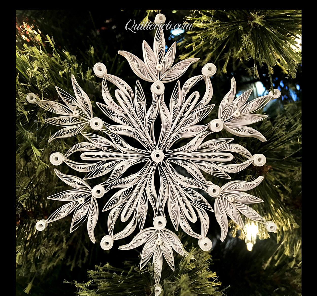 &nbsp;Quilling in white, snowflake design full view against pine wreath backdrop.