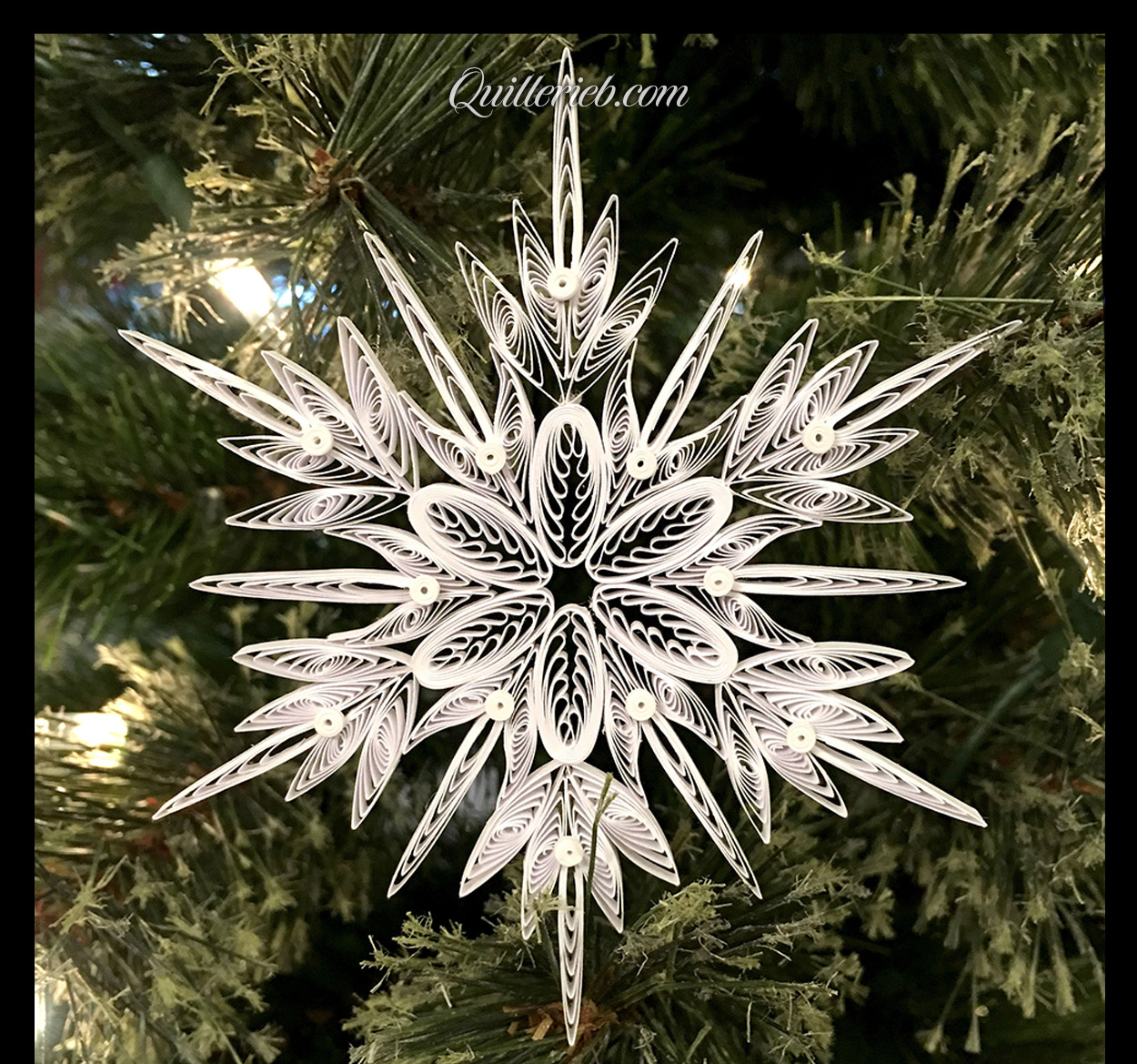 &nbsp;Another quilling in white, snowflake design full view against pine wreath backdrop.