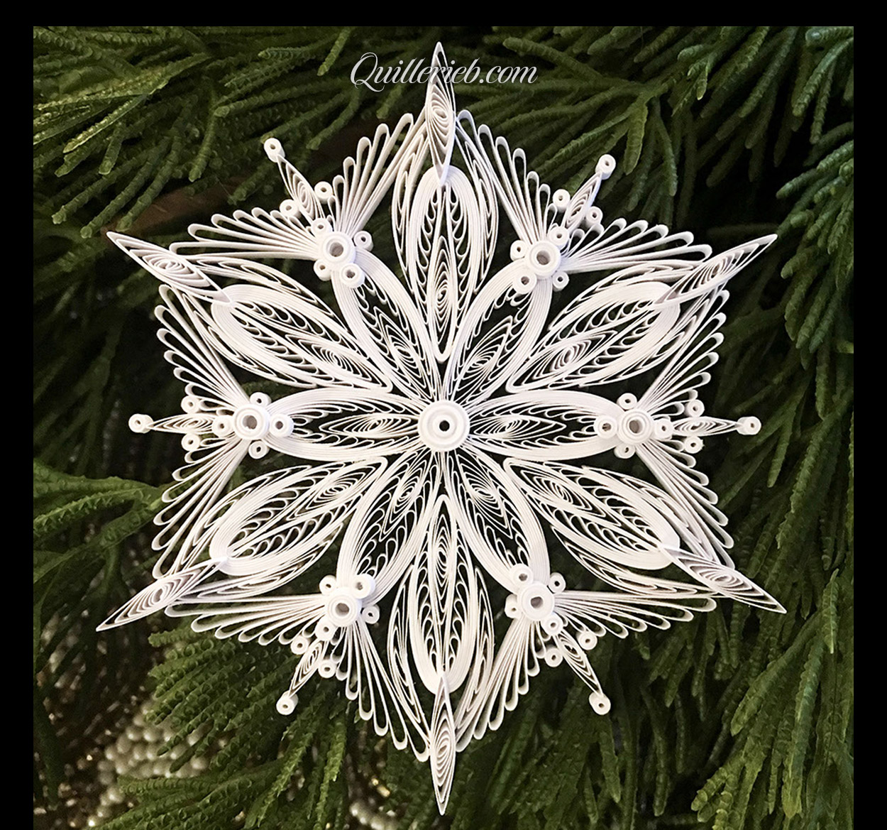 &nbsp;Quilling in white, 4th snowflake design full view against pine wreath backdrop.