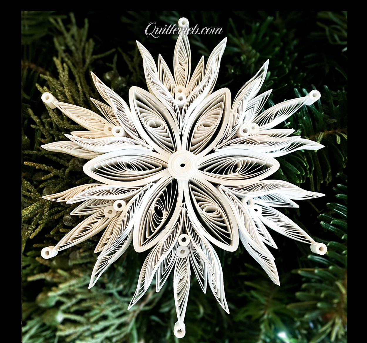 &nbsp;Quilling in white, 5th snowflake design full view against pine wreath backdrop.
