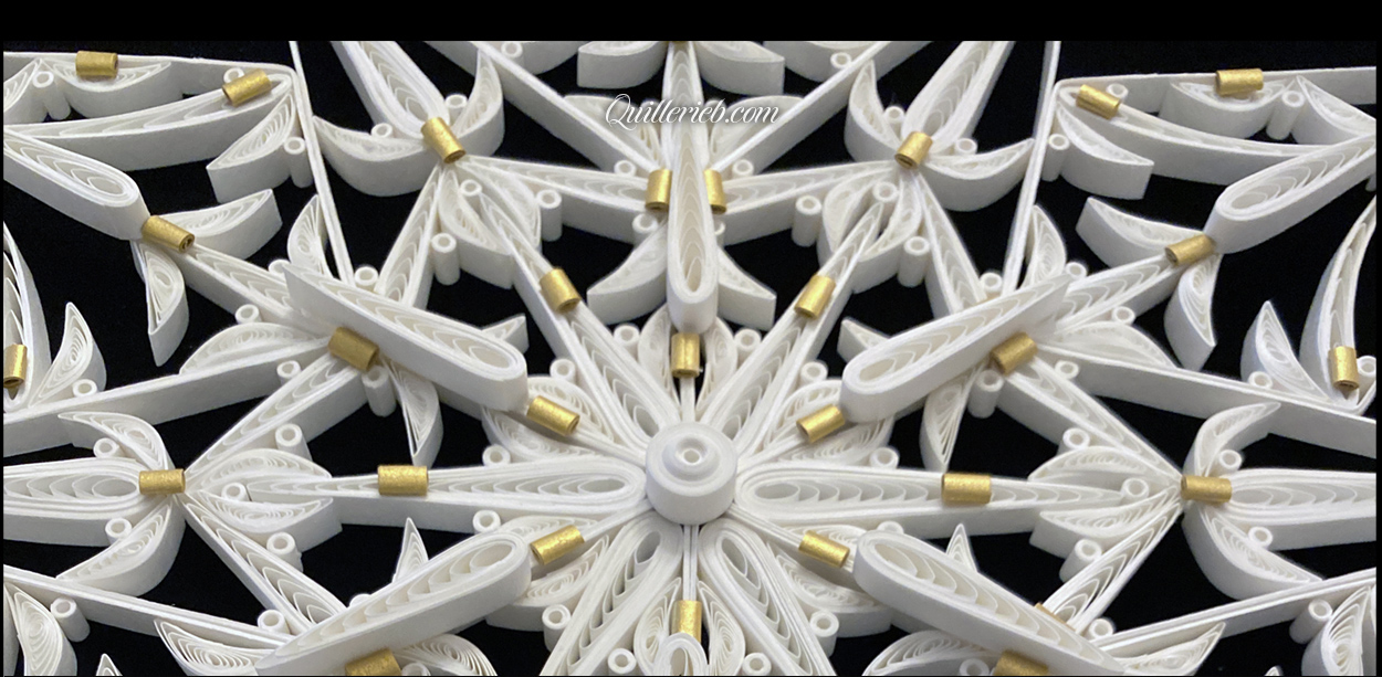 12-Point Star quilling design in white with touches of gold tones above center very close-up view.